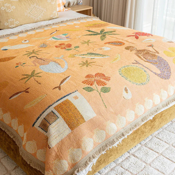 Decorative blanket with floral and nature-themed patterns on a bed in a bedroom.