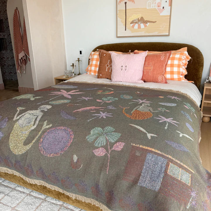 Bedroom with a colorful quilt featuring mermaid designs, pillows, and a painting on the wall.