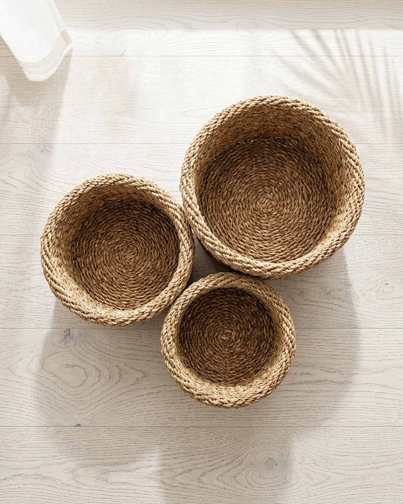Three round woven natural fiber baskets in different sizes arranged on a light wood floor with soft shadows.