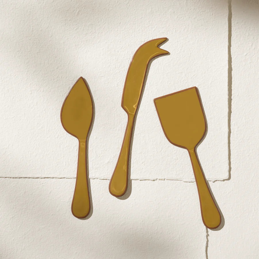 Three gold cheese knives on a textured white surface