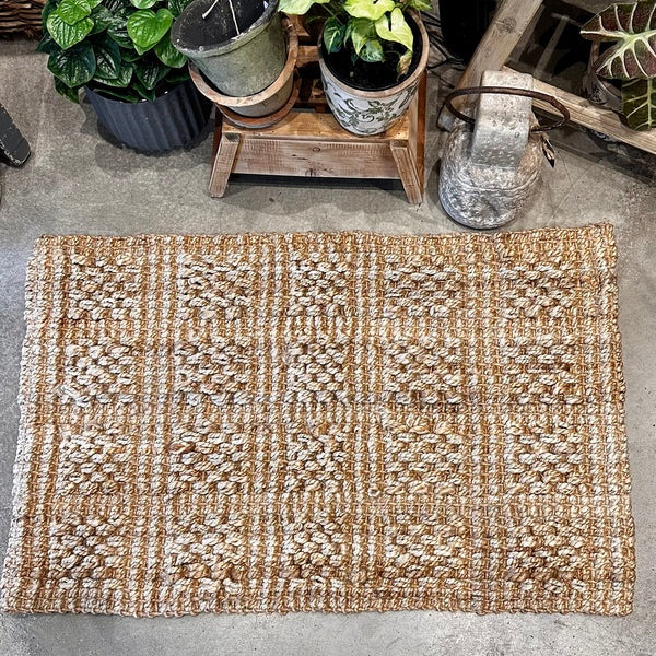 Textured doormat on a concrete floor with potted plants in the background