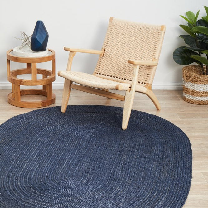 Navy blue round rug on a wooden floor with a wicker chair and side table.