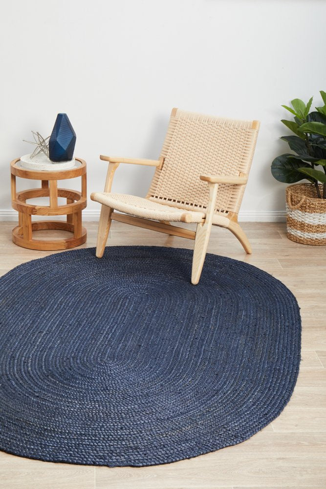 Navy blue round rug on a wooden floor with a wicker chair and side table.