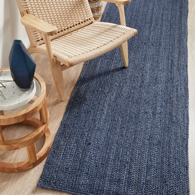 Woven blue rug on a wooden floor with a wicker chair and side table.