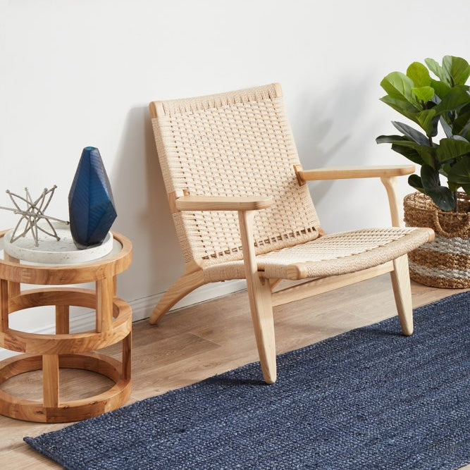 Nautical-themed room with a woven chair, side table, and blue rug.
