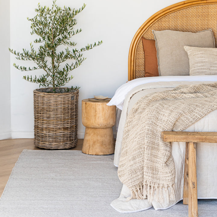 Bedroom with wicker headboard, wooden side table, and potted plant.