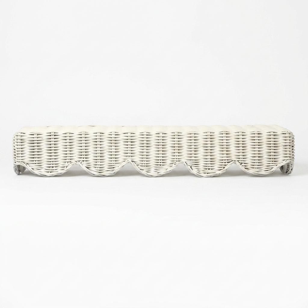 A long, low wicker bench upholstered in an off-white fabric, featuring a scalloped wicker trim along the front and small dark metal feet at the corners, shown against a plain white background.