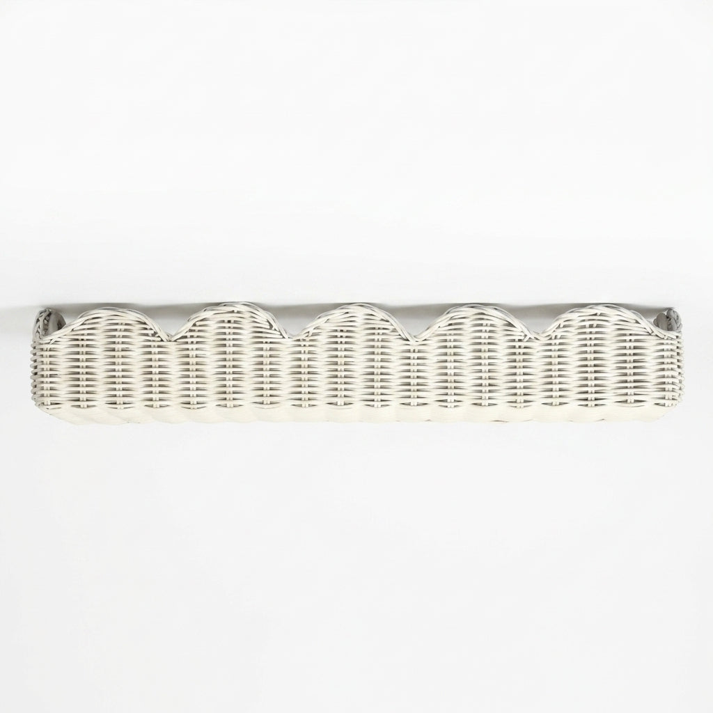 A long, low wicker bench upholstered in an off-white fabric, featuring a scalloped wicker trim along the front and small dark metal feet at the corners, shown against a plain white background.