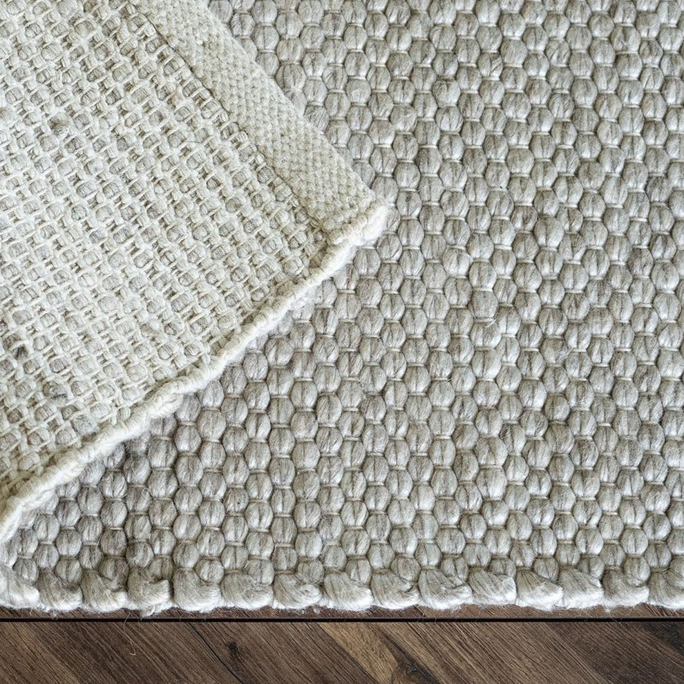 Textured beige rug with a woven pattern on a wooden floor