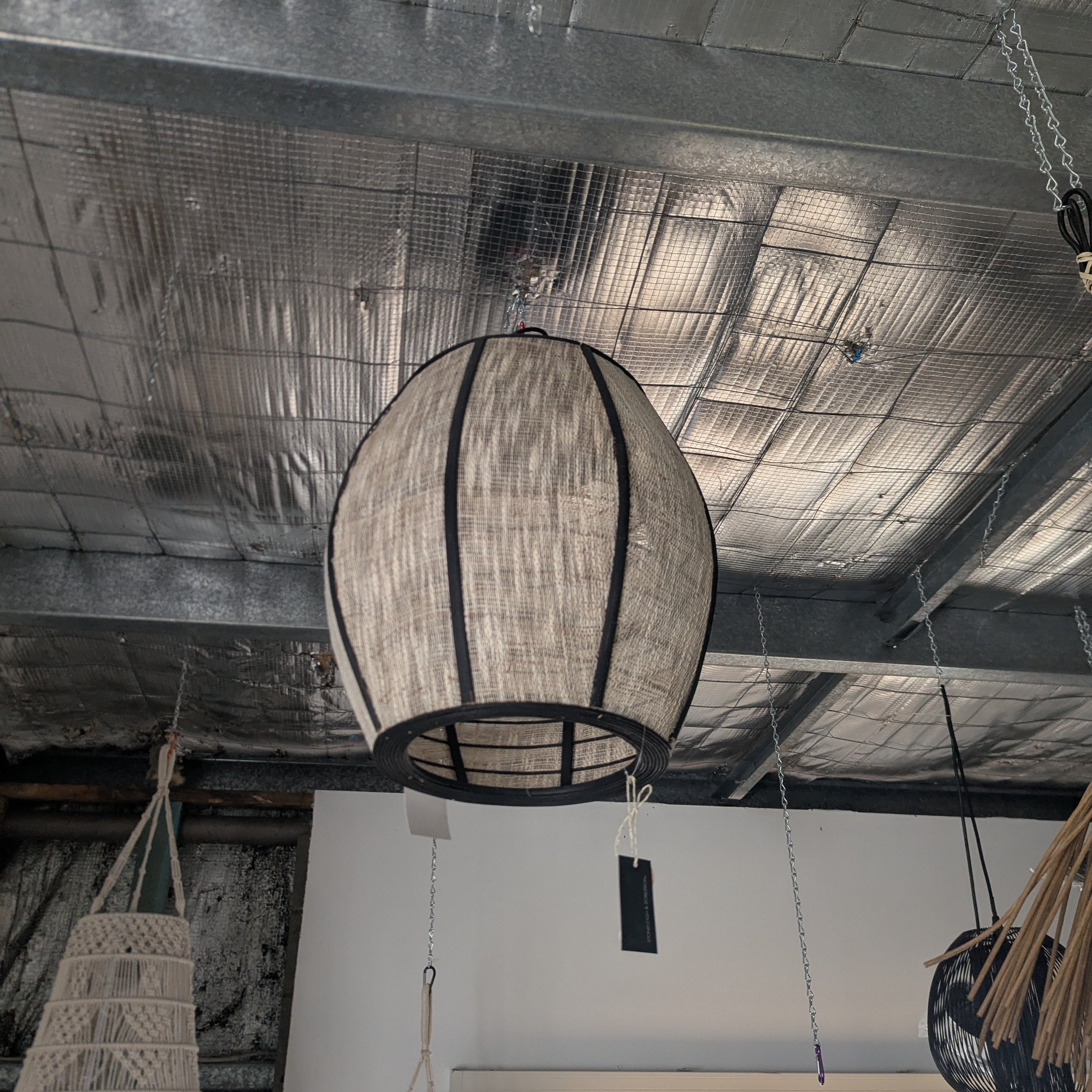 A large woven spherical pendant light hanging from chains in a rustic indoor space with a textured metallic ceiling.
