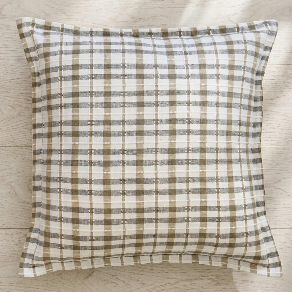 A square throw pillow with a brown and off-white plaid pattern, resting on a light wood floor.