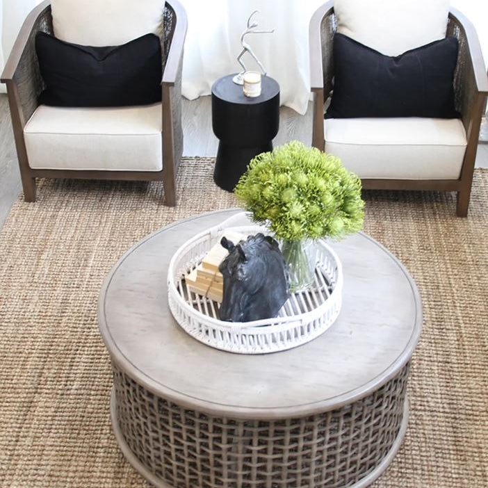 Round wicker coffee table with decorative items in a living room setting.