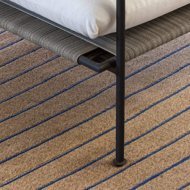 Close-up of a textured carpet with a chair leg on a striped patterned floor.