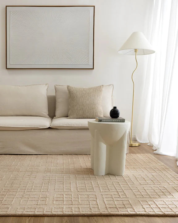 Modern living room with beige sofa, rug, and side table.
