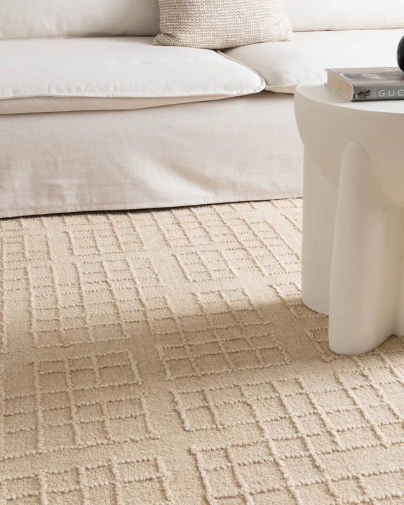 Beige patterned carpet in a living room setting with a sofa and coffee table.