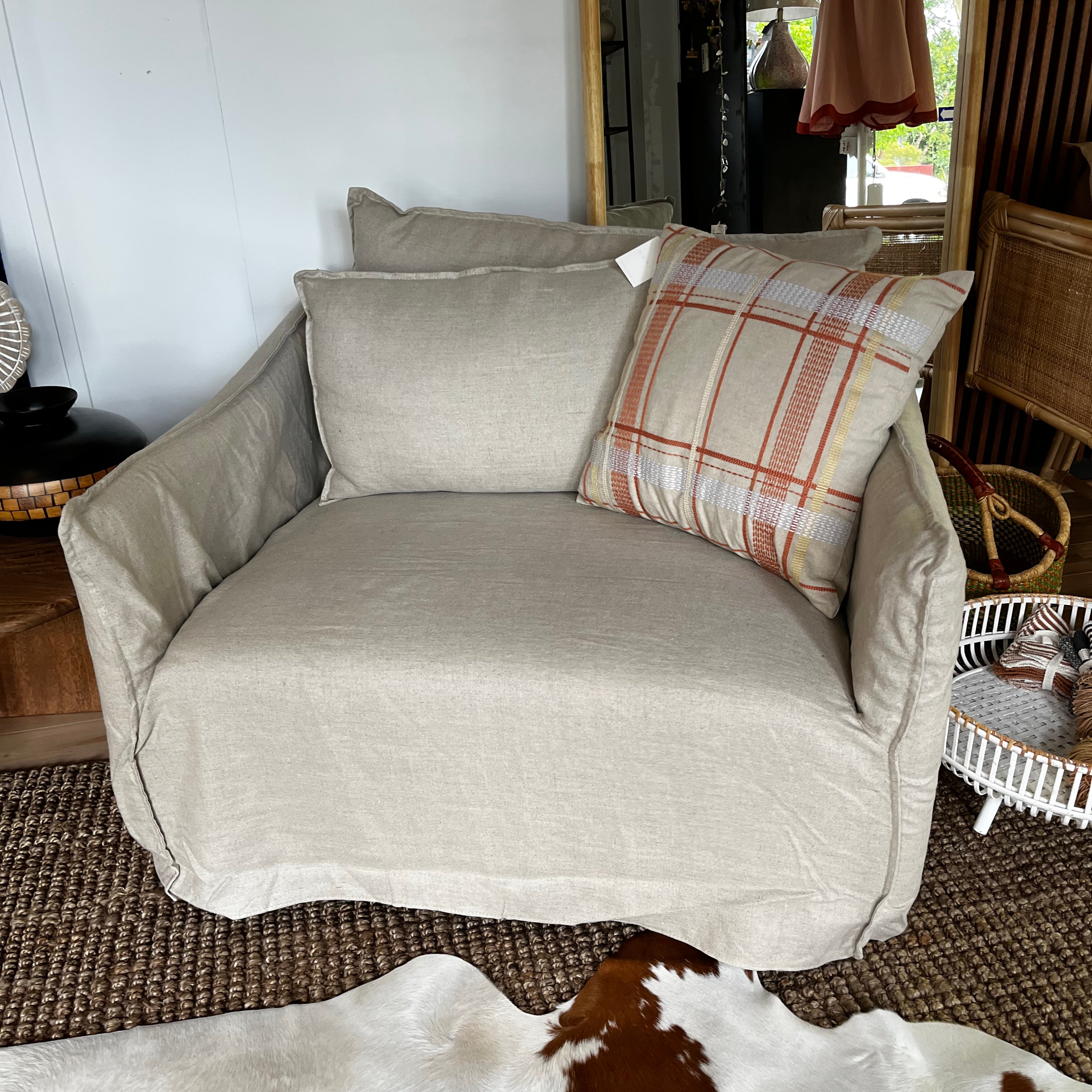 Beige sofa with plaid pillow in a room with wicker furniture and cowhide rug