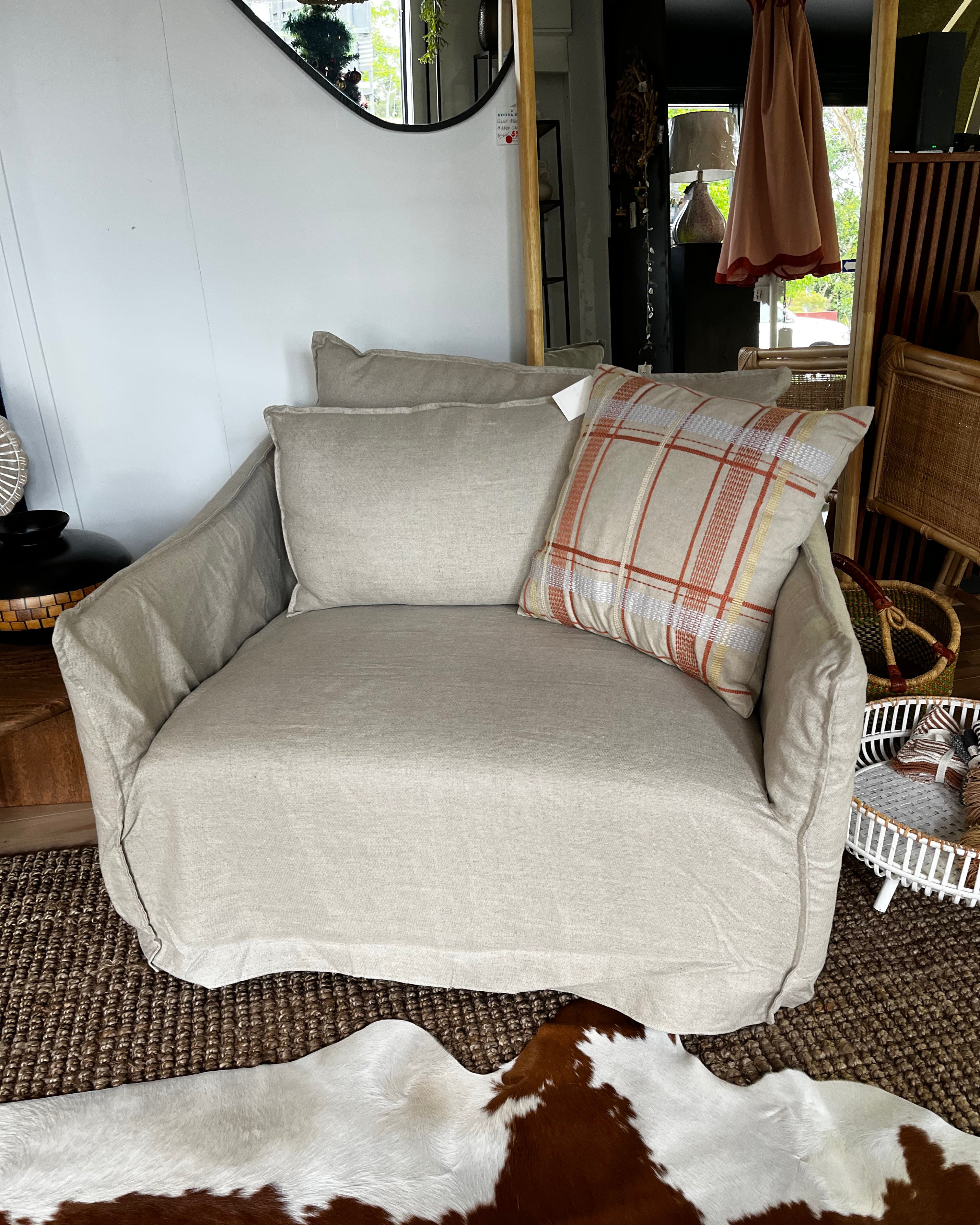 Beige sofa with plaid pillow in a room with wicker furniture and cowhide rug