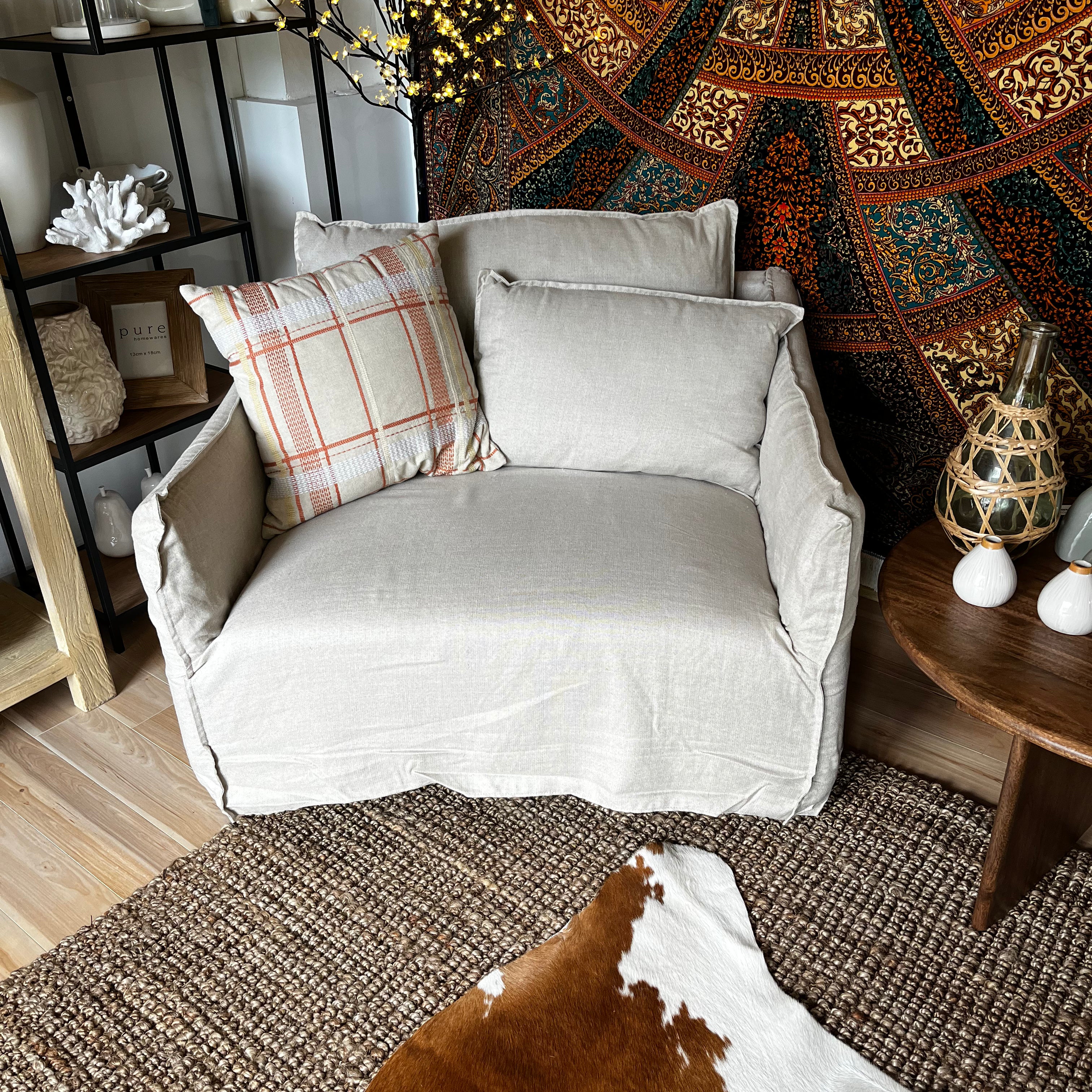 Gray armchair with plaid pillow in a room with patterned tapestry and wooden furniture.
