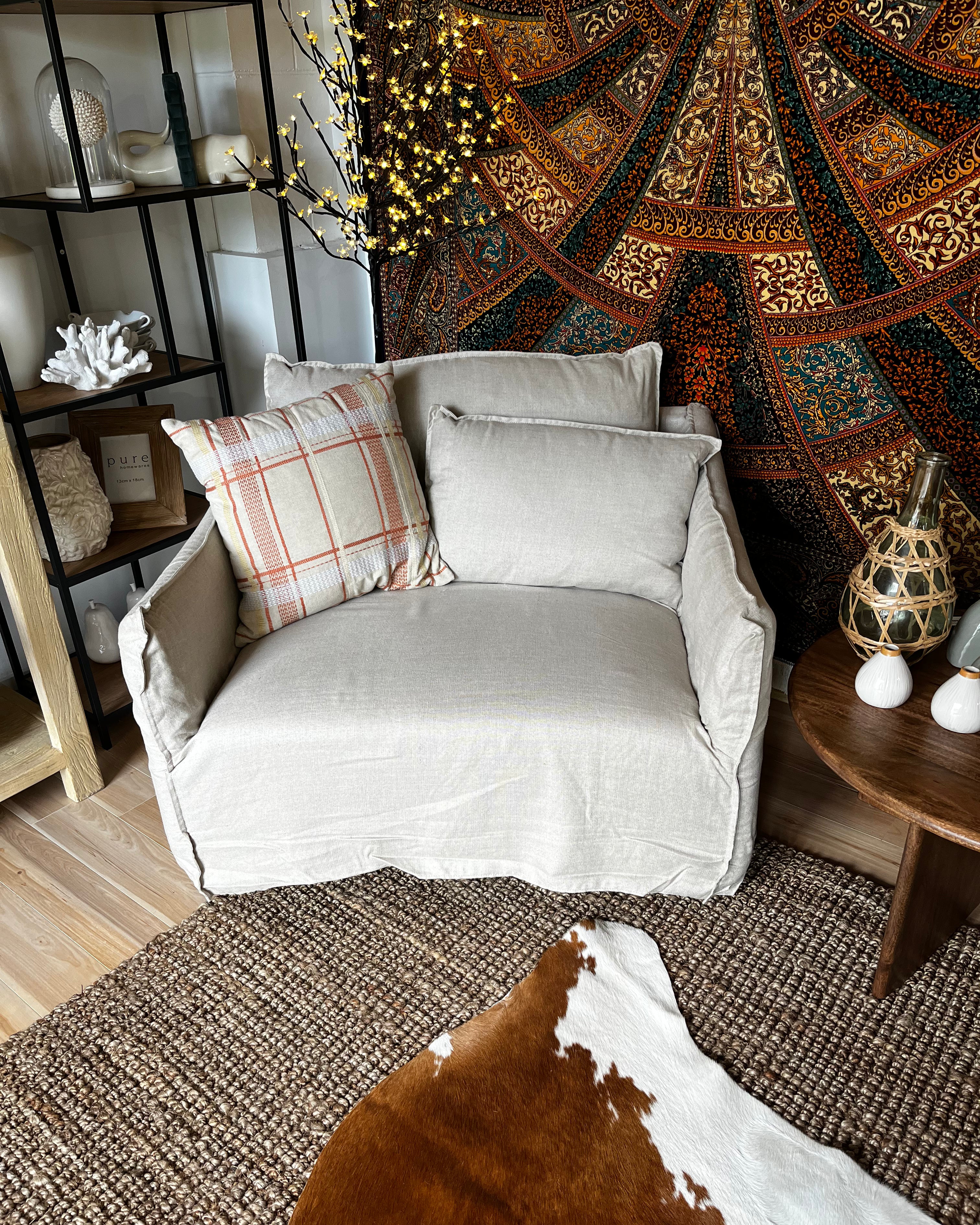 Gray armchair with plaid pillow in a room with patterned tapestry and wooden furniture.