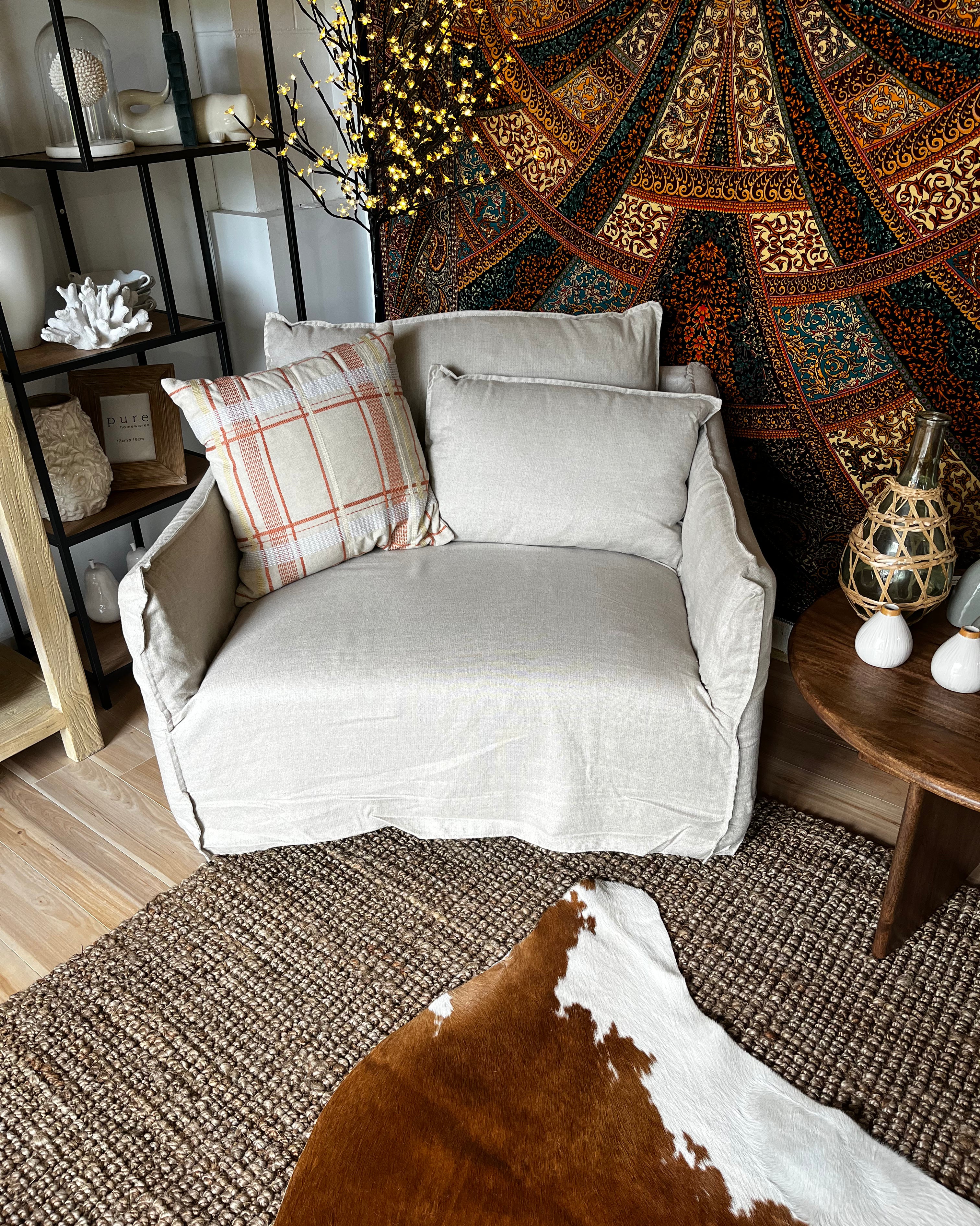 Gray armchair with plaid pillow in a room with patterned tapestry and wooden furniture.