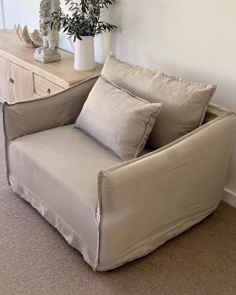 Beige armchair with cushions in a room with a wooden sideboard and decorative items.