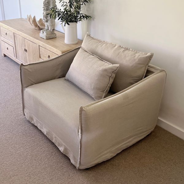Beige armchair with cushions in a room with a wooden sideboard and decorative items.