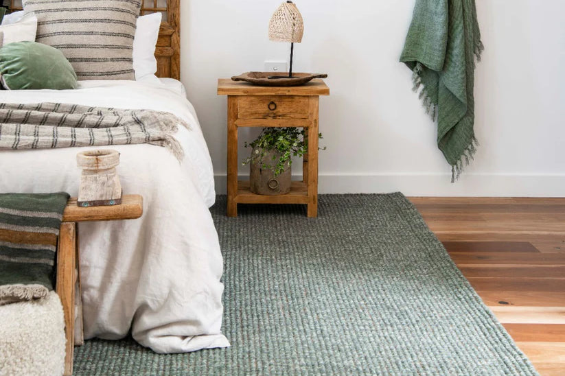 Cozy bedroom with a green rug, wooden nightstand, and bed with striped pillows.