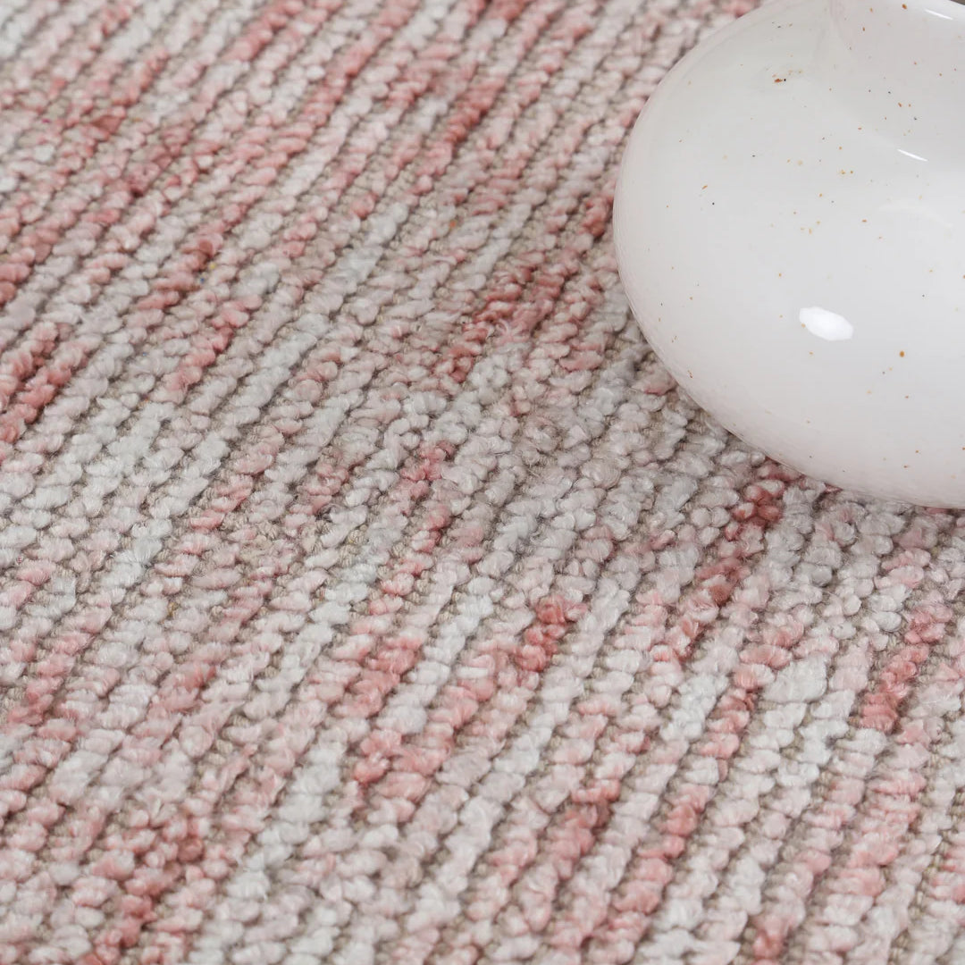 Close-up of a textured pink and beige carpet with a white ceramic vase.