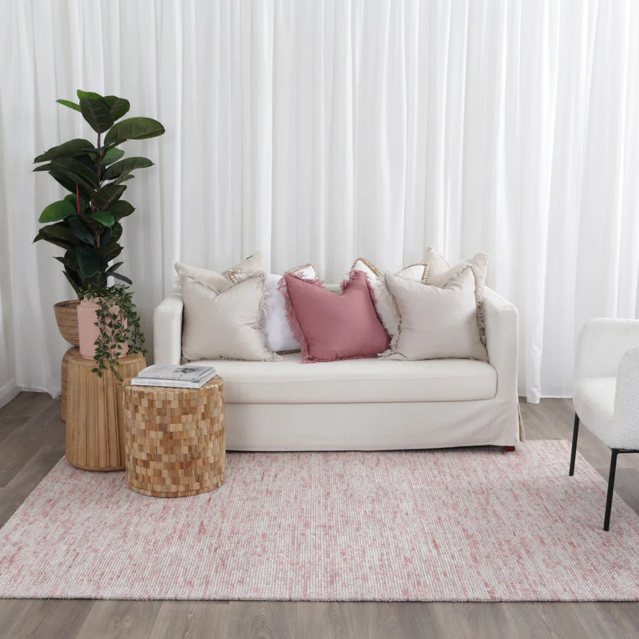 Living room with a beige sofa, pink cushions, and a plant on a wooden side table.