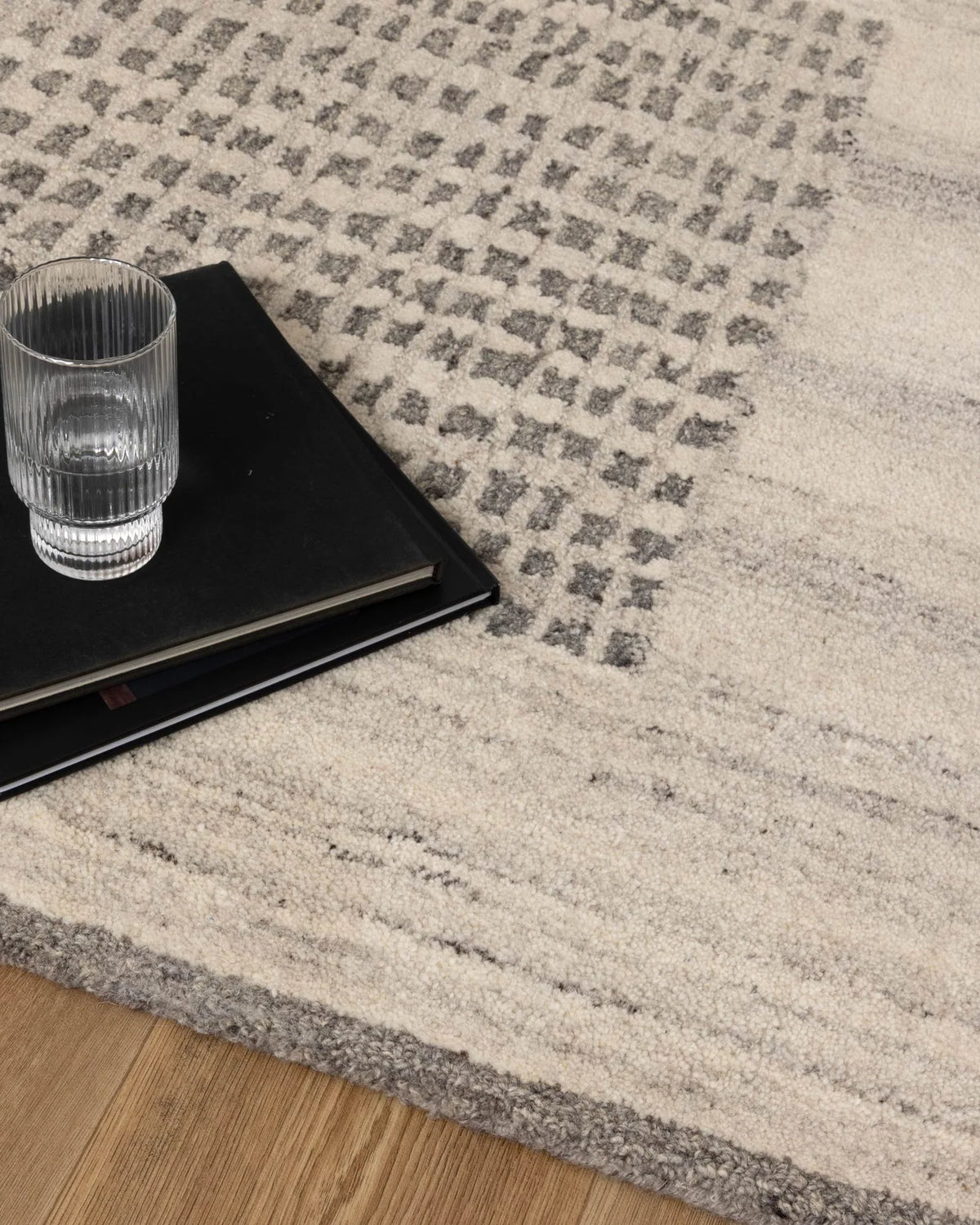 Glass of water and black book on a textured gray and beige rug