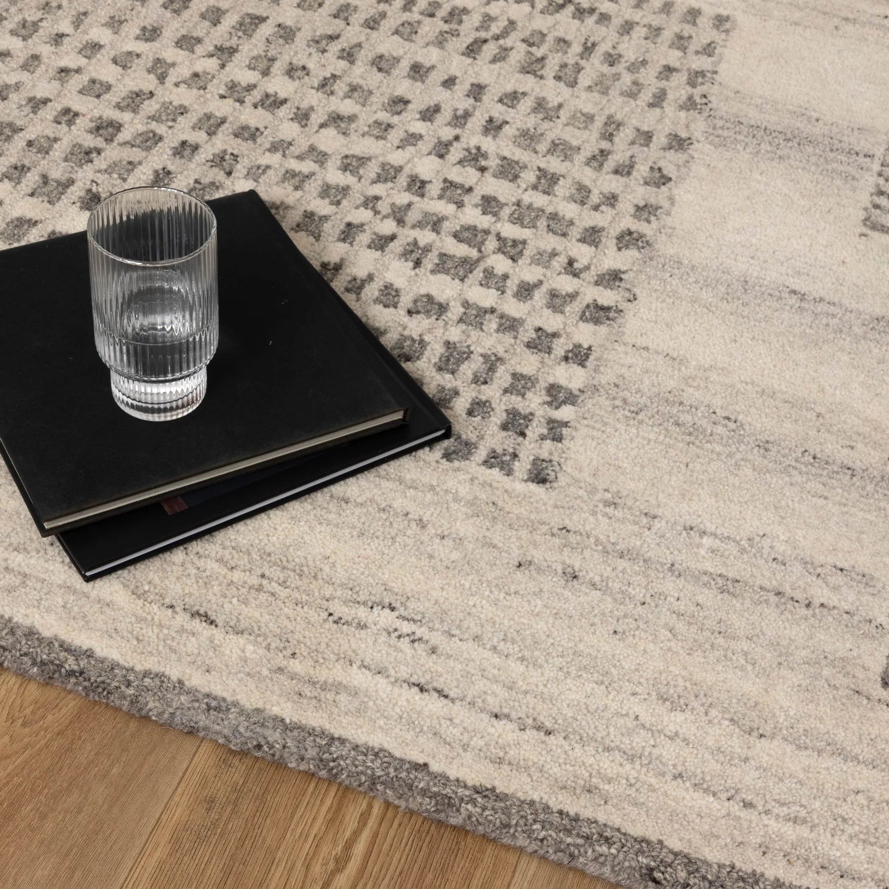 Glass of water and black book on a textured gray and beige rug