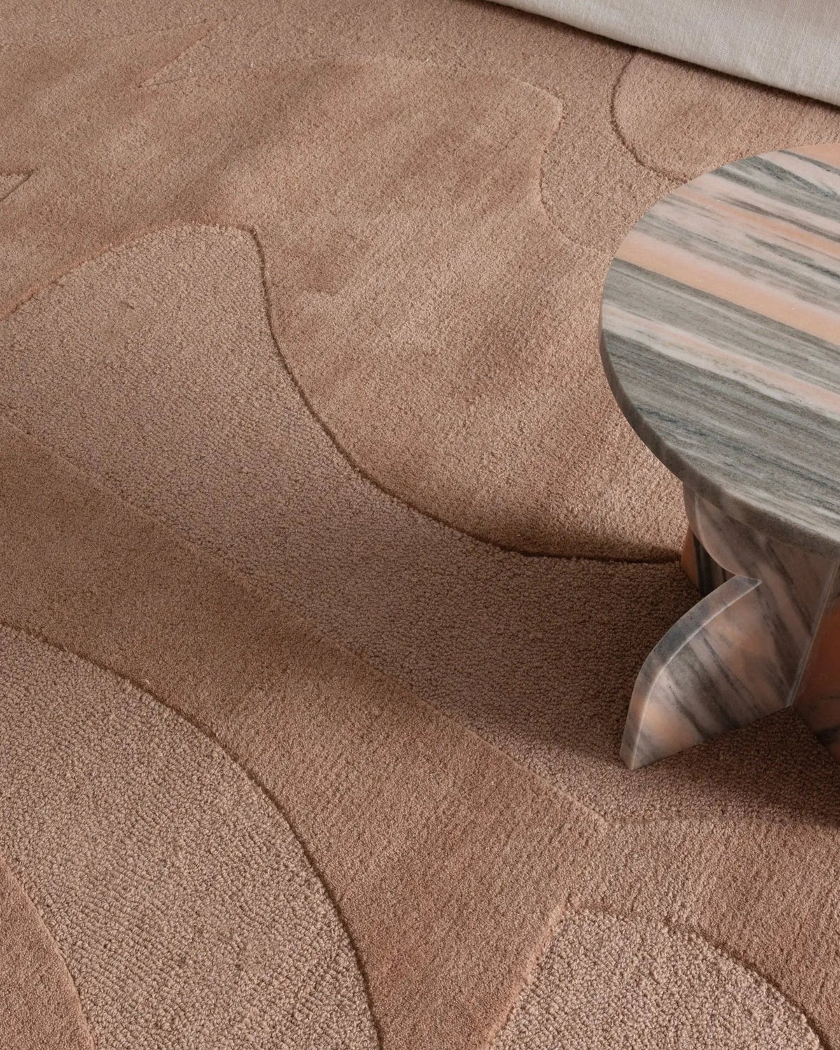 Close-up of a textured beige carpet with a small wooden stool featuring a marble pattern.