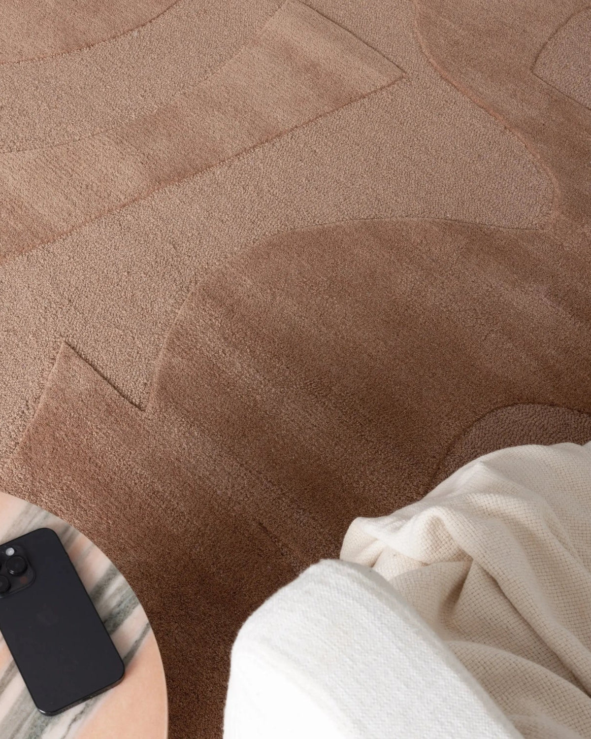Person sitting on a brown textured rug with a phone beside them