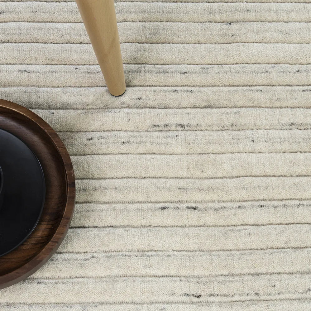 Close-up of a textured beige rug with a wooden chair leg and woven basket.