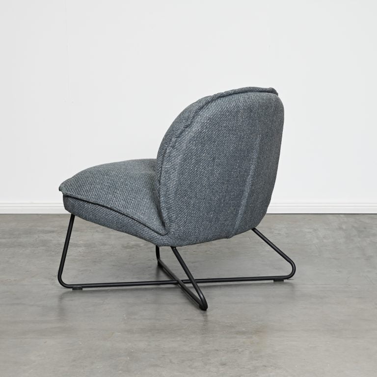 A modern gray upholstered accent chair with a black metal sled base, shown in a minimalist room setting with a concrete floor and white wall.