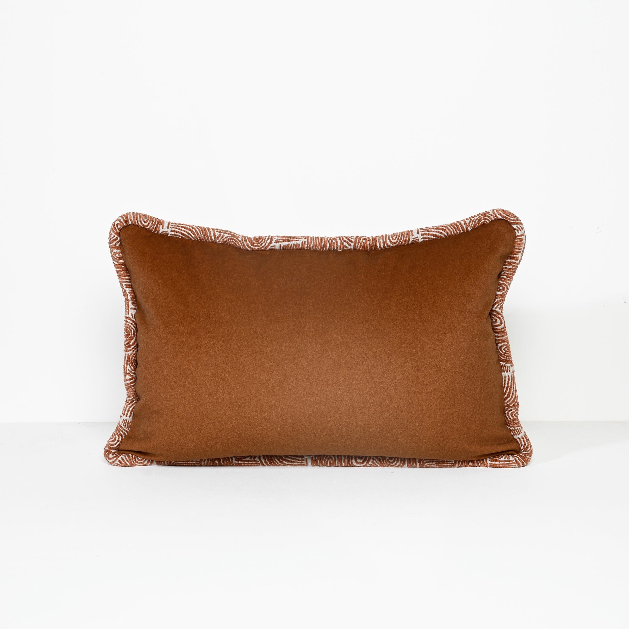A rectangular brown throw pillow with a patterned piped border, photographed against a clean white background.