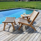 Wooden outdoor furniture set with a chair, ottoman, and small table by a pool.