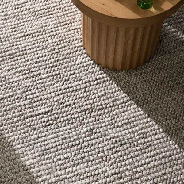 Small wooden table with a book and green glasses on a textured gray carpet