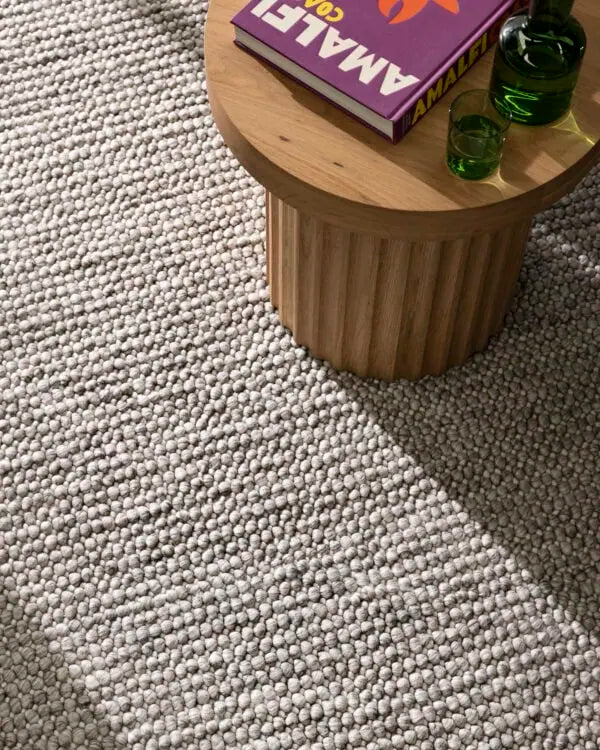 Small wooden table with a book and green glasses on a textured gray carpet