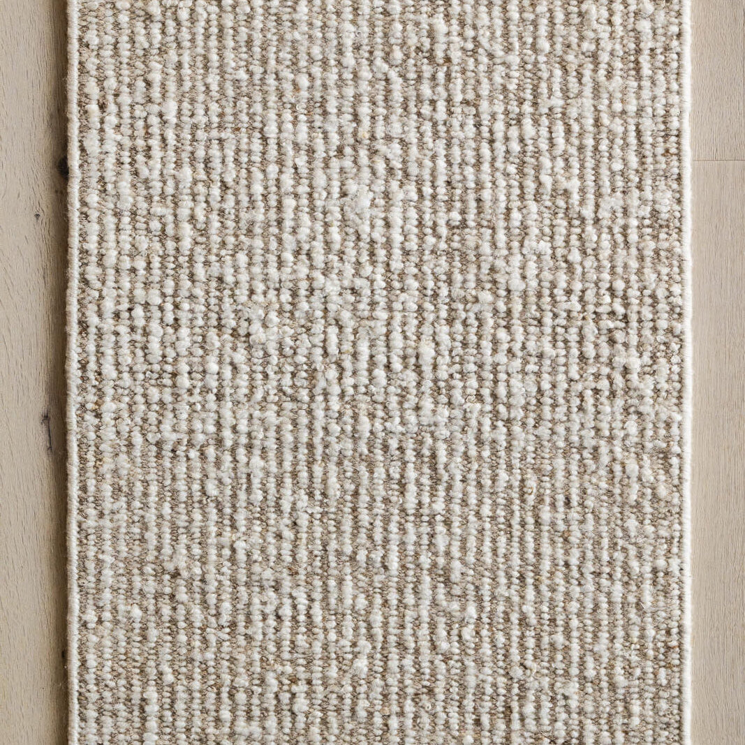 Textured area rug with a natural color palette on a wooden floor.