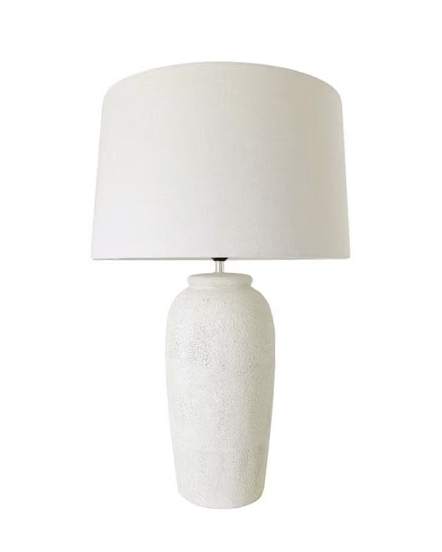 A table lamp with a textured white ceramic base and a matching white fabric drum shade, shown against a plain white background.