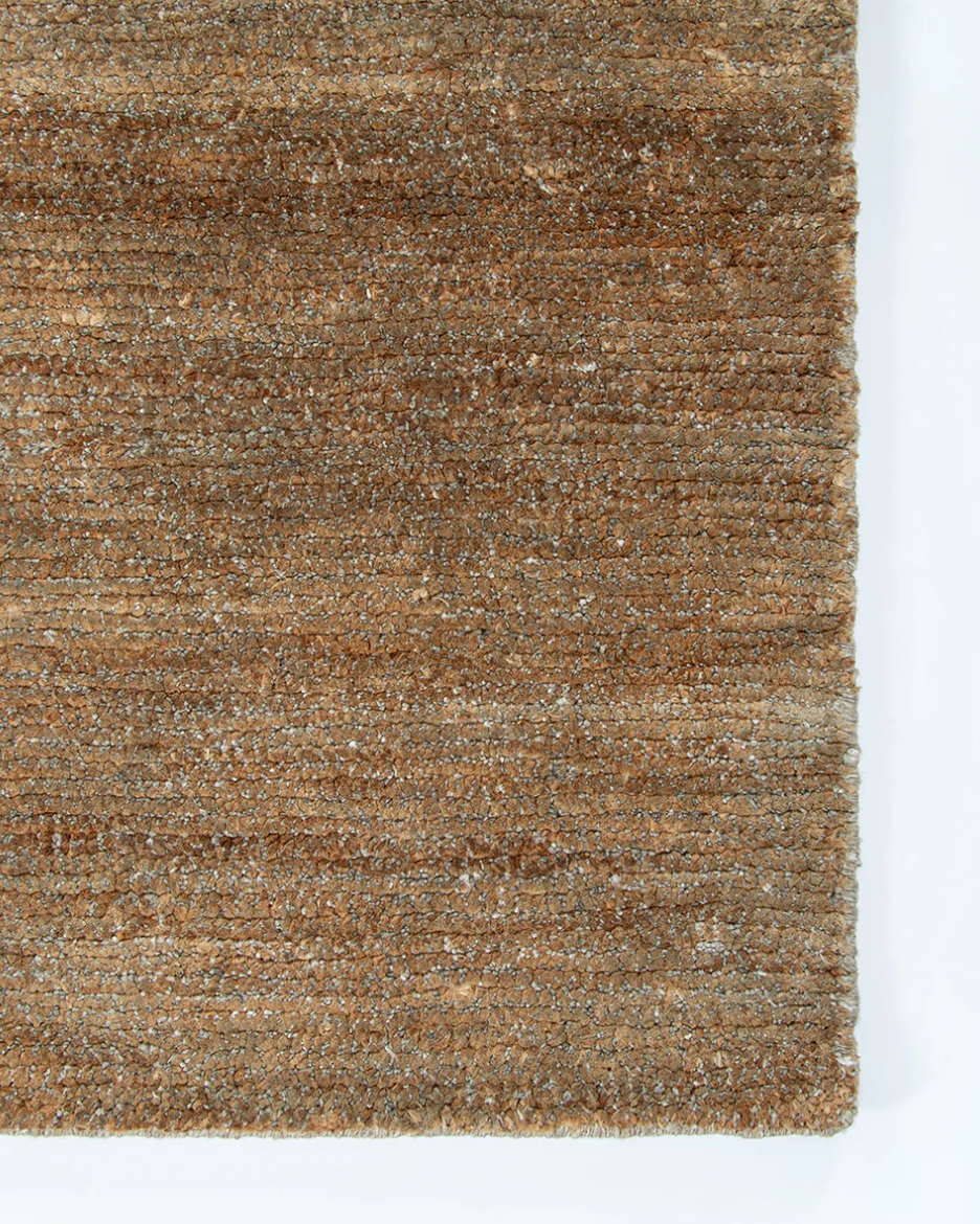 A close-up of a textured woven rug or fabric in earthy brown and tan tones, shown against a white background.