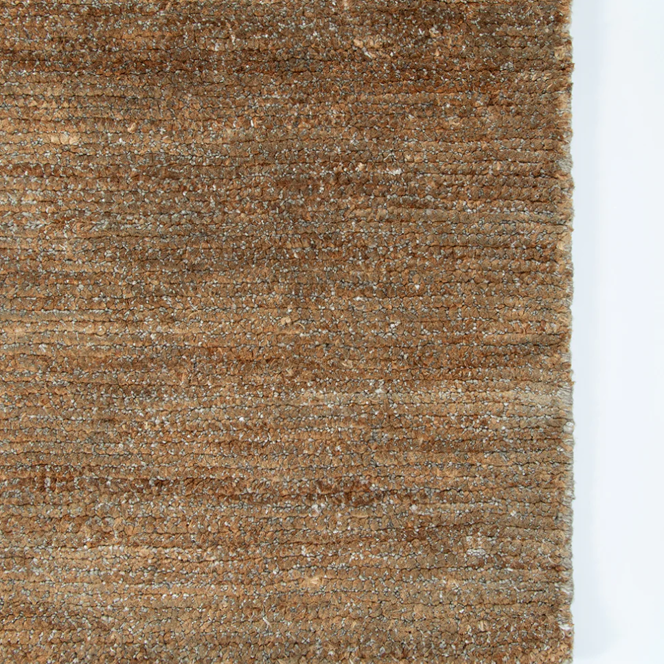 A close-up of a textured woven rug or fabric in earthy brown and tan tones, shown against a white background.