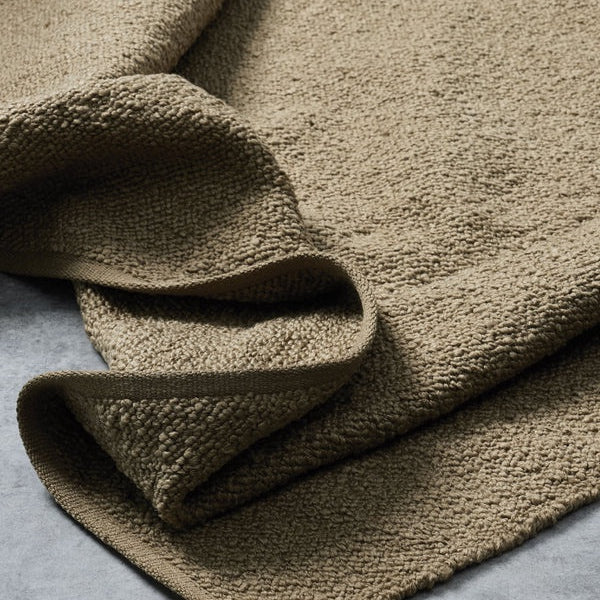 A close-up of a folded, textured woven fabric in a warm taupe-brown color, showing its chunky knit pattern against a neutral gray background.