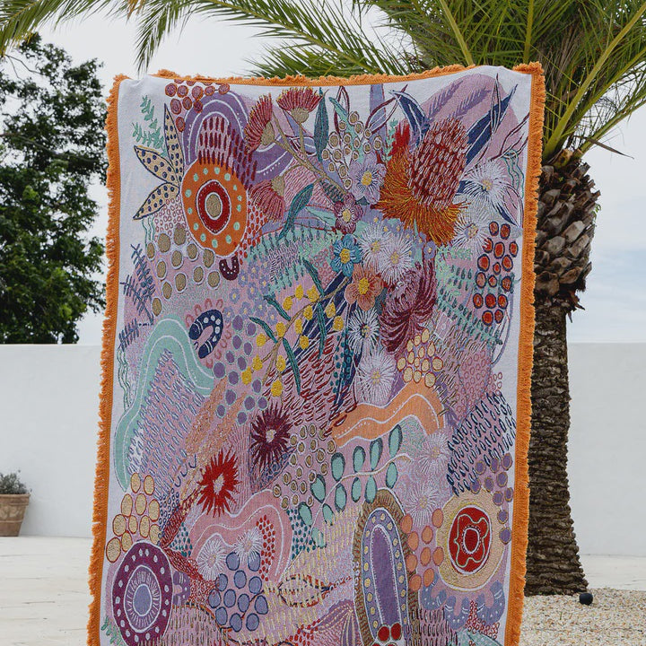 Colorful patterned blanket on a wooden floor with palm trees in the background