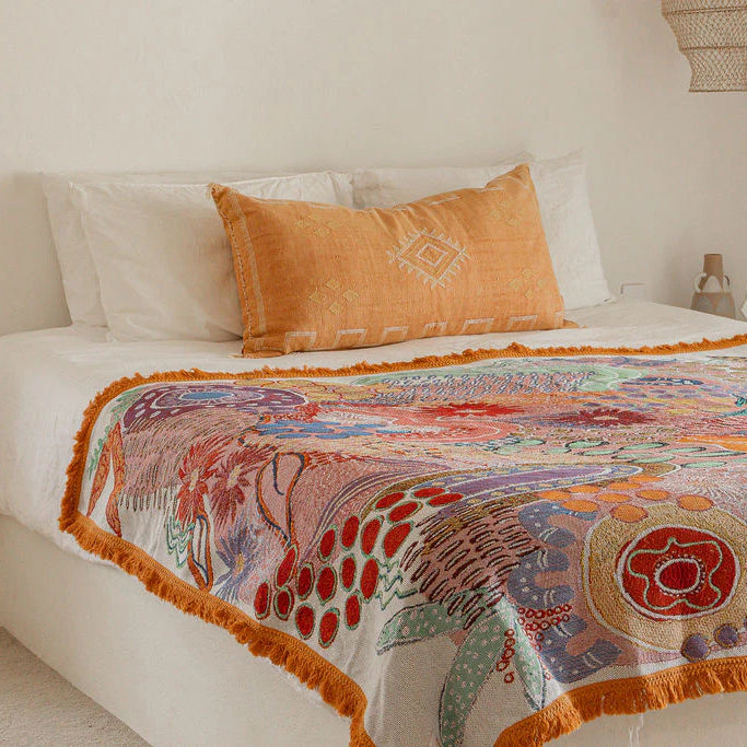 Bed with a colorful patterned throw blanket and an orange pillow.