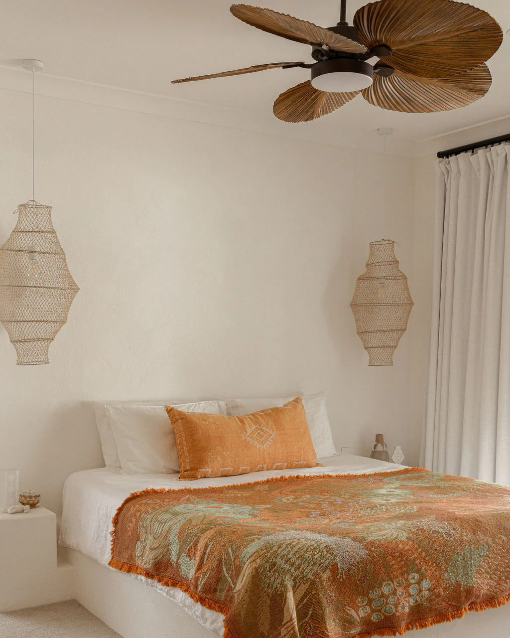 Bedroom with a bed featuring an orange and green blanket, white pillows, and decorative lamps.