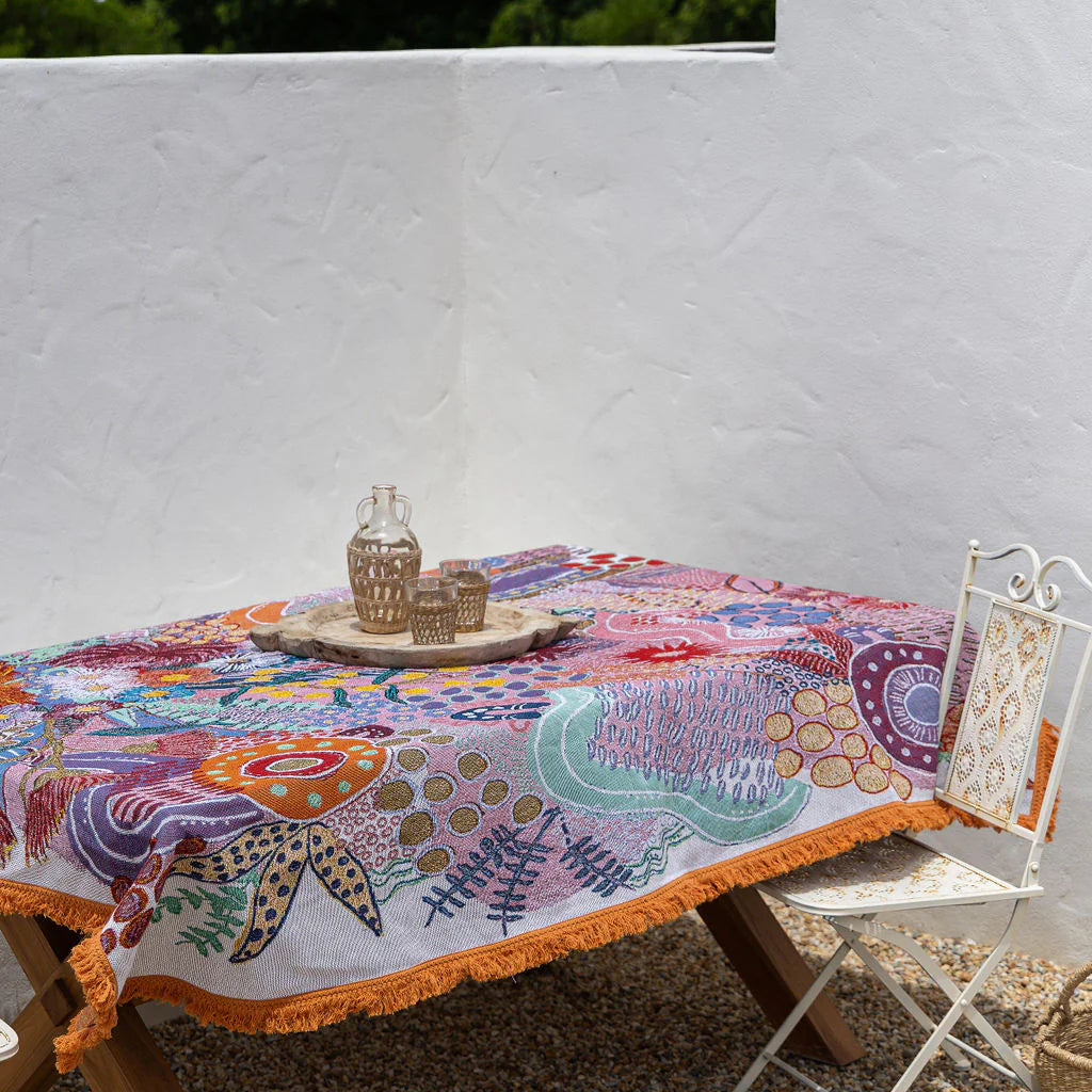 Colorful embroidered tablecloth on a wooden table with a white wall and greenery in the background