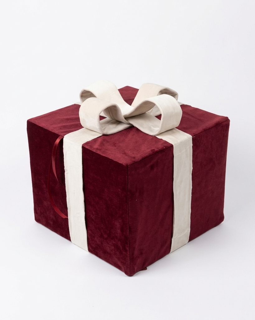 A square gift box wrapped in deep burgundy velvet fabric with a cream-colored satin ribbon and bow, set against a plain white background.