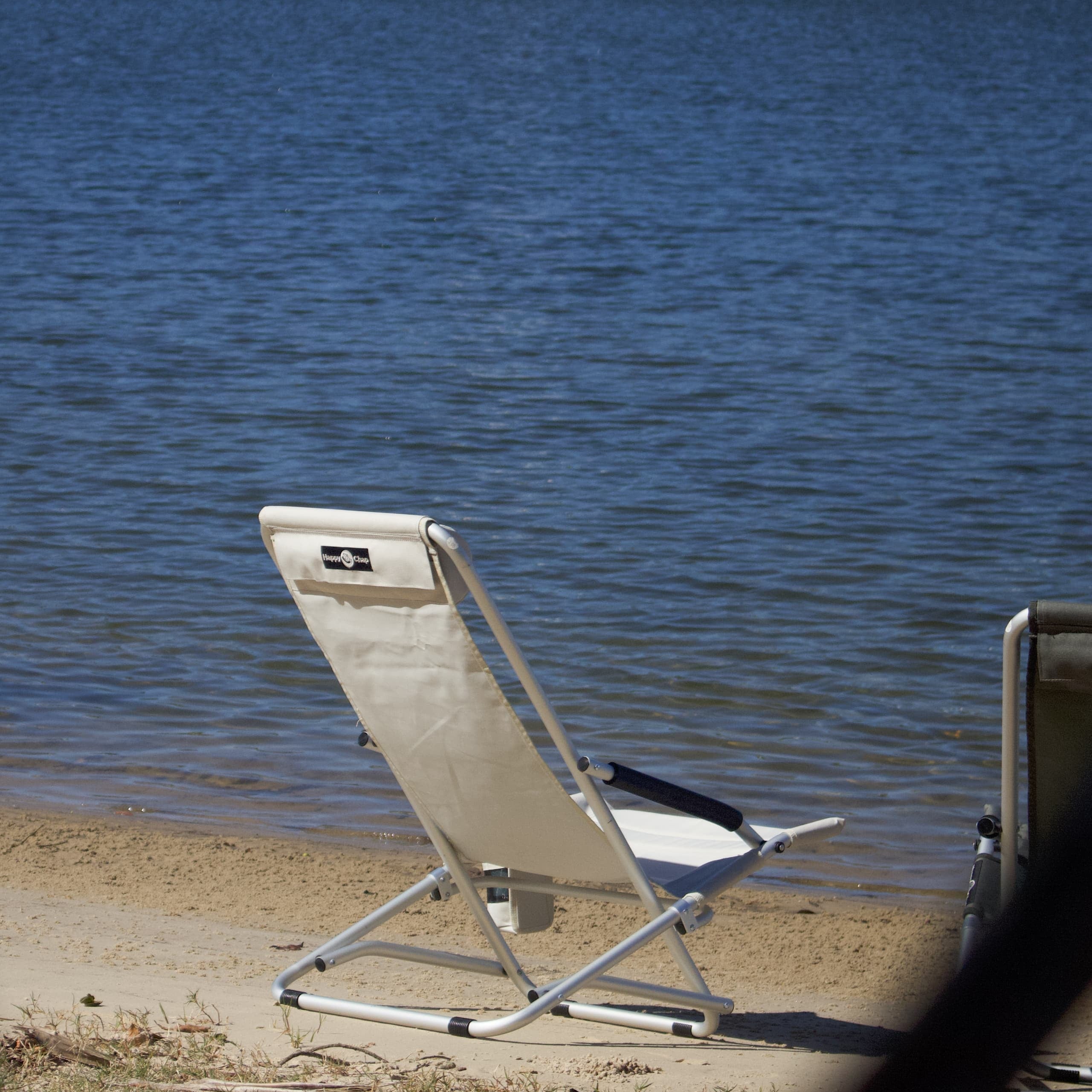 Beige folding chair on a sandy beach with water in the background